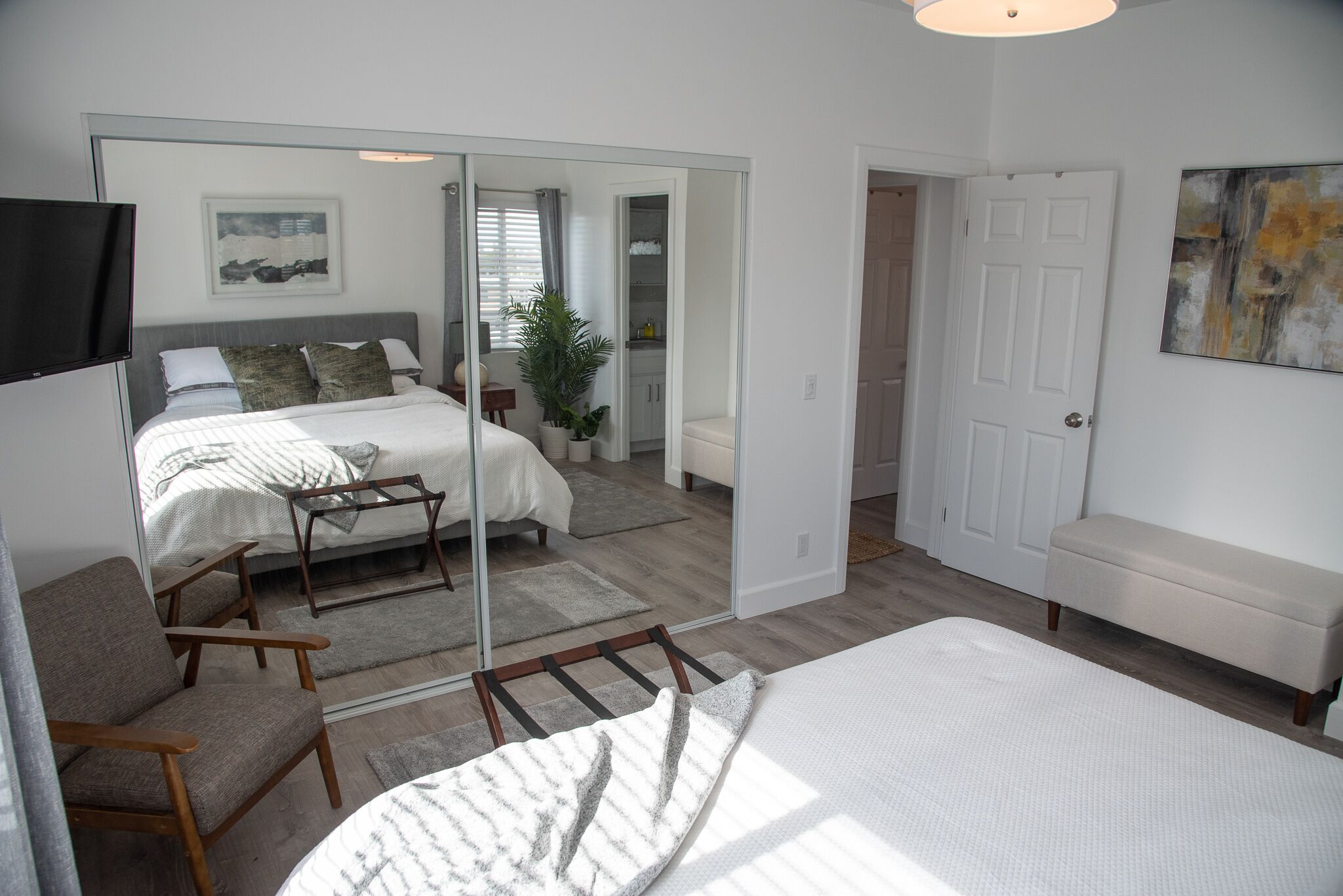 Une chambre moderne avec un grand lit, un coin salon comprenant un fauteuil, une petite table et un miroir.