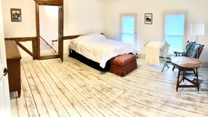 Un dormitorio con suelo de madera, una cama con cubrecama blanco, una silla de madera y una mesita.