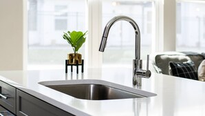 A modern kitchen with a stainless steel sink, a potted plant, and a view of the city through large windows. - Duke9 ~ Private Penthouse Rooftop ~ Newly Redesigned Interior ~ 8 Min to Downtown and Broadway (Nashville)