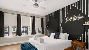 A modern bedroom with a bed, a tufted bench, a nightstand, and a wall with a drip paint design. - Duke9 ~ Private Penthouse Rooftop ~ Newly Redesigned Interior ~ 8 Min to Downtown and Broadway (Nashville)