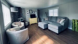 Un salon moderne avec un canapé d’angle, un fauteuil blanc, une commode jaune et un mur d’accent en pierre.