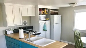 Une cuisine avec des meubles blancs, un îlot central bleu doté d’un évier, une cuisinière et un réfrigérateur.