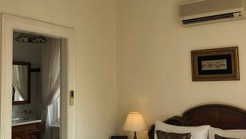 A hotel room with a bed, a chandelier, an air conditioner, a bedside lamp, and a framed picture on the wall.