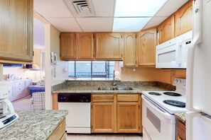Compact kitchen with a stove, microwave, and dishwasher, featuring a granite countertop and a window.