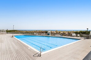 Relax by the serene pool surrounded by a deck, lifeguard chair, and simple fence, with a tranquil beach view.