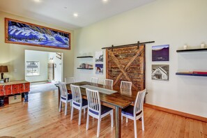 Un coin repas avec une table en bois et des chaises blanches, une grande peinture au-dessus, et un panneau mural en bois.