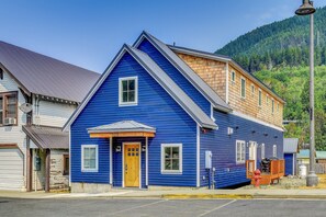 Une maison à deux étages, avec une façade bleue, une porte d’entrée en bois et un garage apparent.