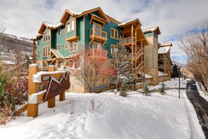 A multi-story building with a green facade and wooden balconies, surrounded by snow-covered ground and a clear sky. - Private Hot Tub|Walk to Town Lift and Main Street | Managed by Park City Lodging (Park City)