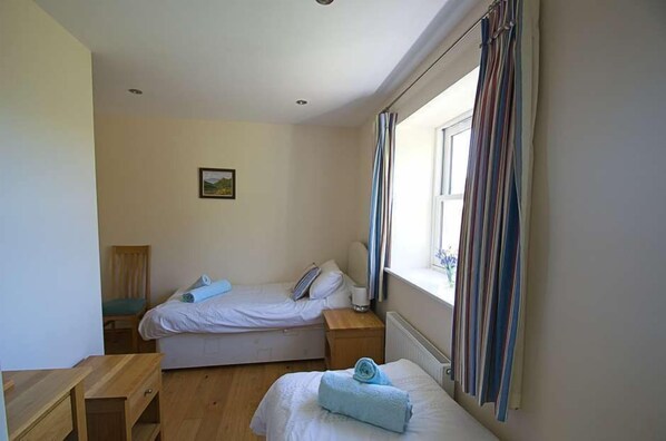 A bedroom with two single beds, a wooden chair, a small table, and a window with curtains.