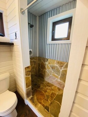 A bathroom with a stone shower enclosure, a toilet, and a window above the shower.