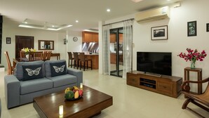 A modern living room with a sofa, coffee table, TV, and a dining area in the background. - Modern Tropical Villa (Koh Samui)