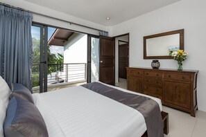 Une chambre avec un grand lit, une commode en bois et une porte-fenêtre coulissante donnant sur un balcon.