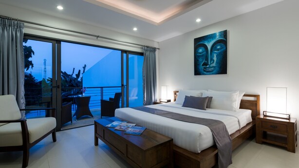 A modern hotel room with a large bed, a sitting area with a coffee table, and a balcony with a view of the ocean. - Modern Tropical Villa (Koh Samui)