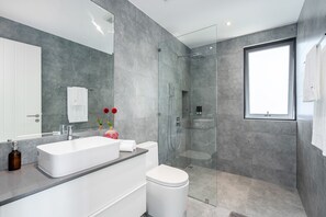 A modern bathroom with a large mirror, white sink, and a glass-enclosed shower.