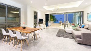 A modern living room with a wooden dining table, white chairs, a grey sofa, and a TV. - Villa Palm Vista - Luxury, Private Pool Villa (Koh Samui)
