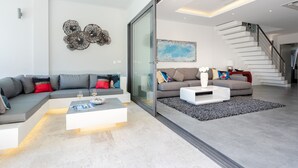 A modern living room with a sectional sofa, a coffee table, and a staircase leading to another level. - Villa Palm Vista - Luxury, Private Pool Villa (Koh Samui)