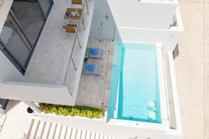 A modern outdoor pool area with a clear view of the pool, lounge chairs, and a small table.