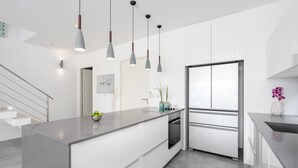 A modern kitchen with white cabinetry, a central island, pendant lighting, and a stainless steel refrigerator. - Villa Palm Vista - Luxury, Private Pool Villa (Koh Samui)