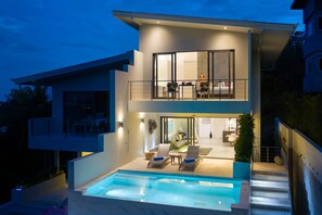 A modern two-story house with a swimming pool, outdoor seating, and a balcony.