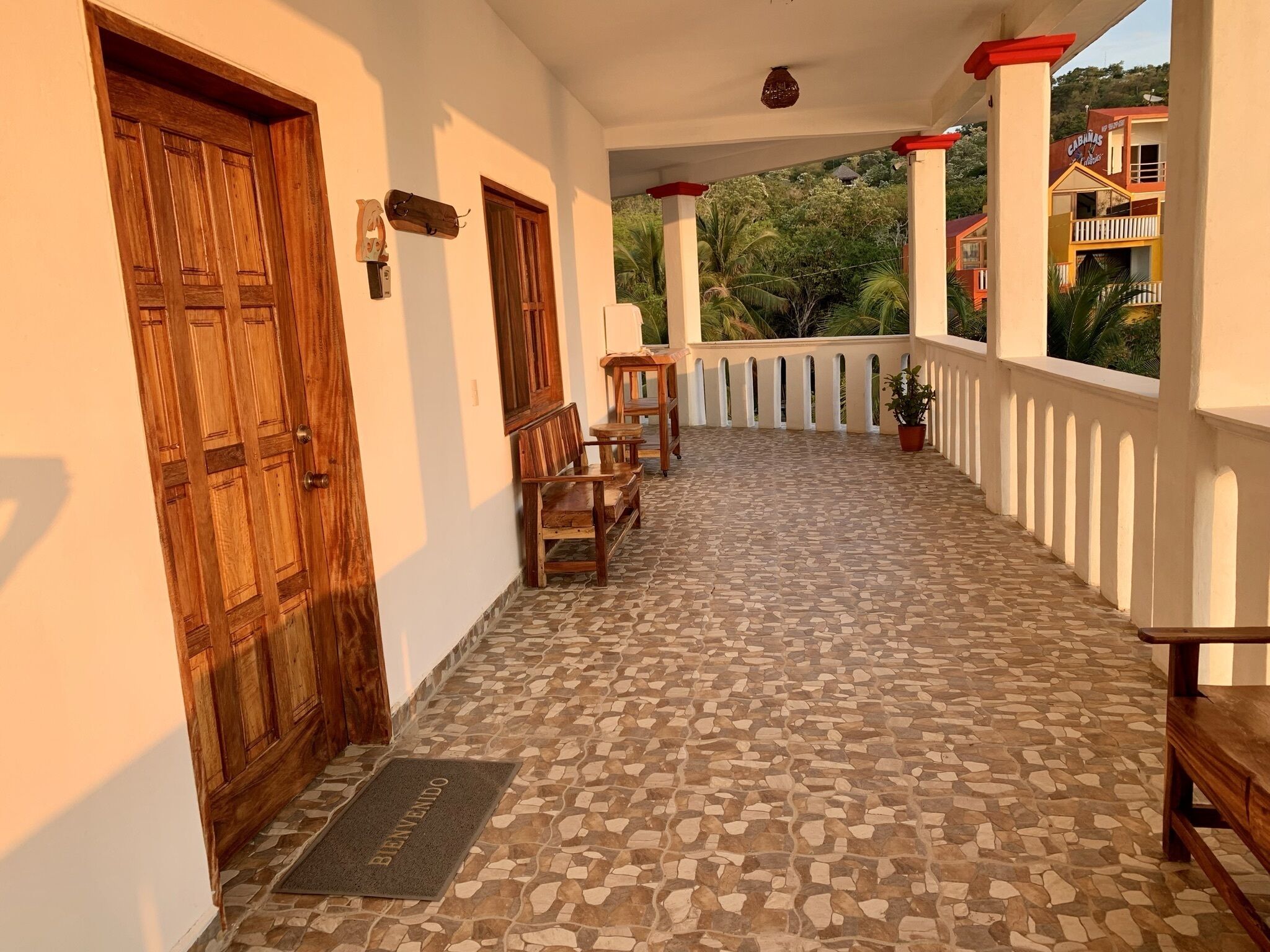 A covered outdoor area with a tiled floor, wooden benches, and a door.