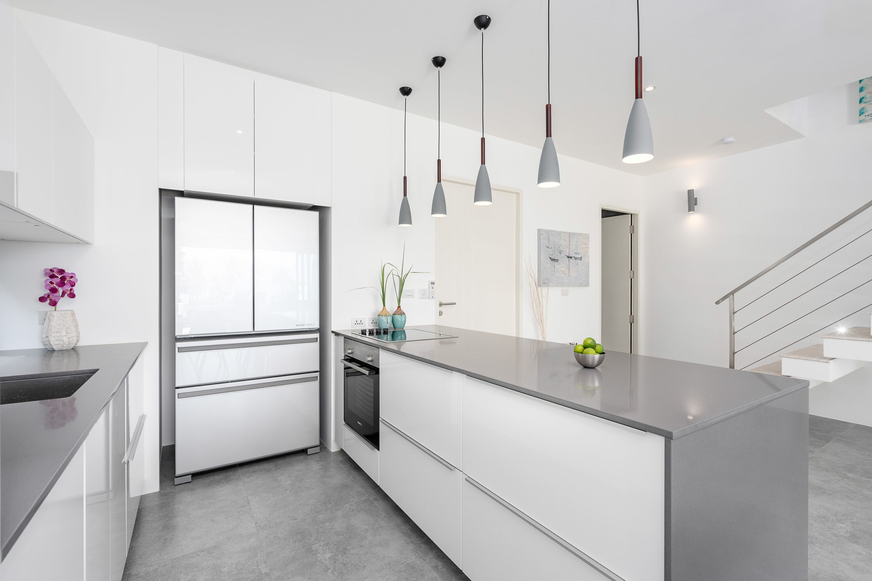 Une cuisine moderne avec des meubles blancs, un four encastré et des luminaires suspendus.