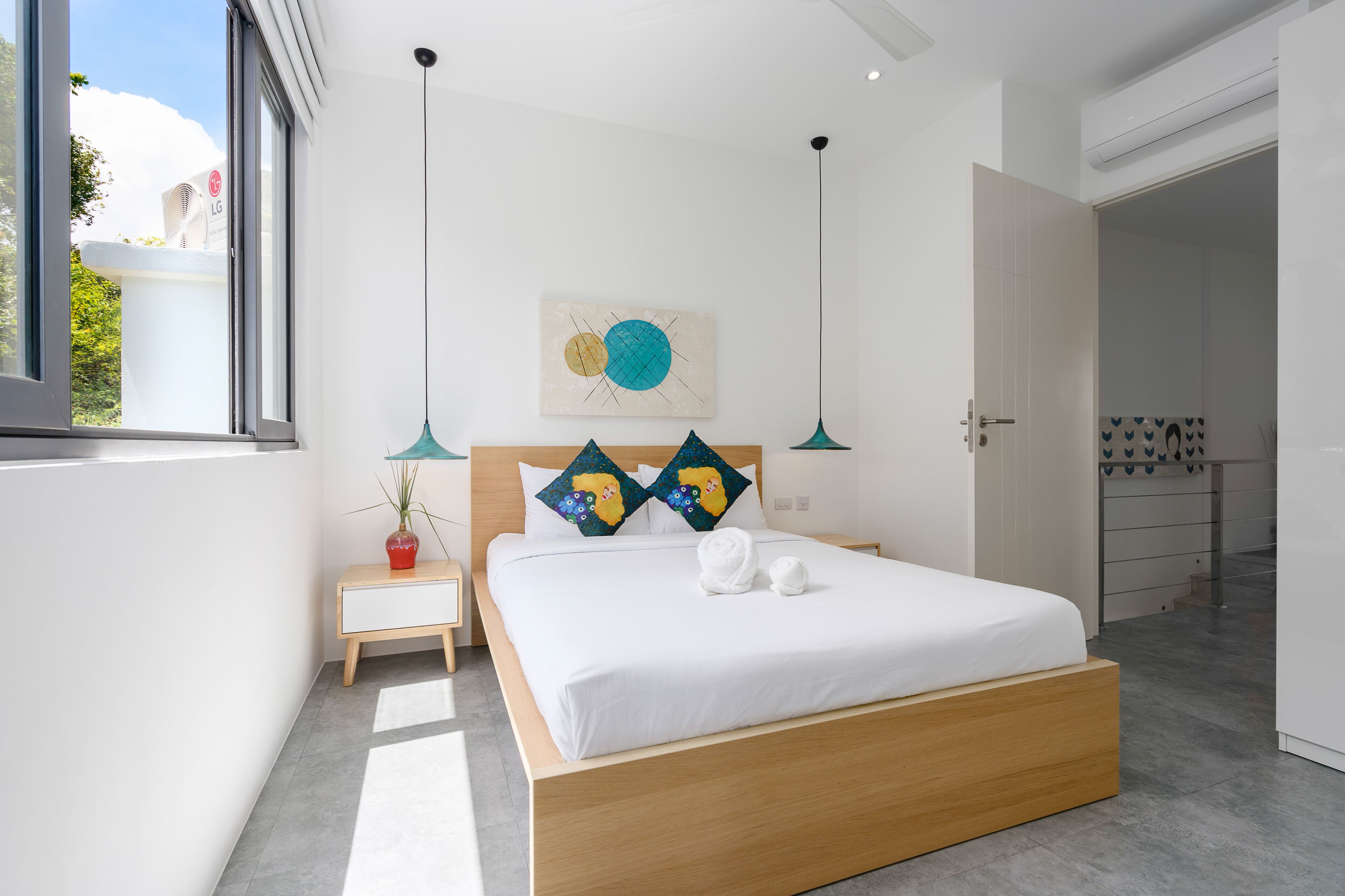 A modern bedroom with a large bed, a bedside table with a lamp, and a window with a view of the outdoors.