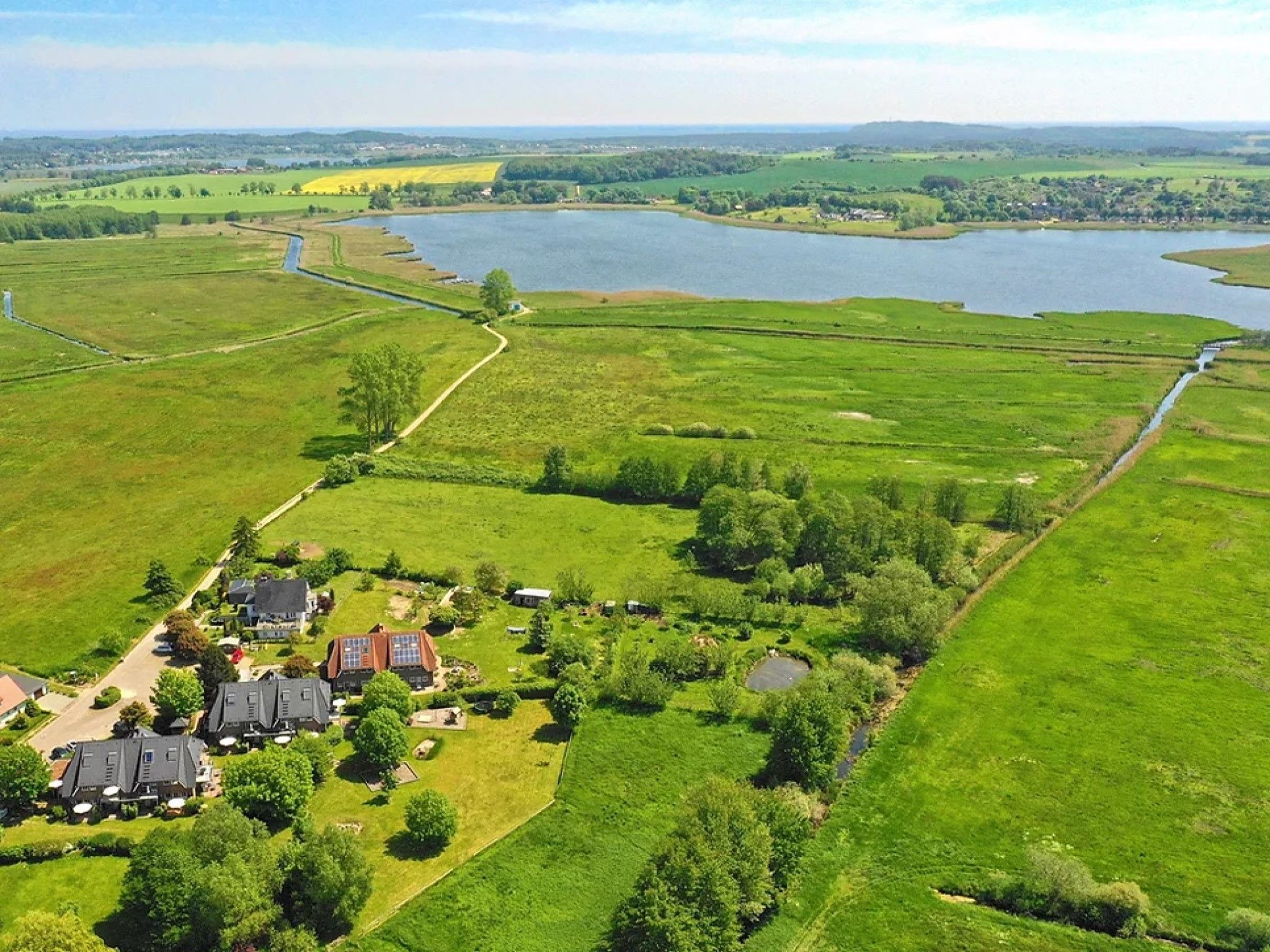 A residential area with houses, a large body of water, and surrounding green fields.