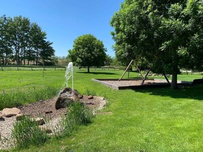 A grassy park area with a water feature, a swing set, and a bench.
