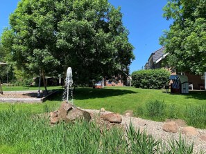 A garden with a fountain, trees, and a small structure with a striped awning.