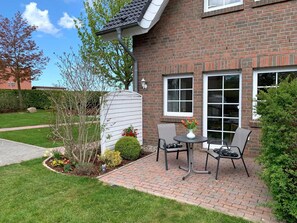 Une maison en briques avec un patio, deux chaises, une table et un vase à fleurs.