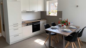 A modern kitchen with white cabinets, a built-in oven, and a dining area with a table set for two. - 2-room apartment 22 (H) - Lancken-Granitz apartment complex (Lancken-Granitz)