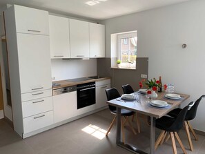 Una cucina moderna con mobili bianchi, forno integrato e zona pranzo con tavolo apparecchiato per due.