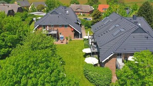 A residential area with houses featuring steep roofs and brick exteriors, surrounded by lush greenery and open fields. - 2-room apartment 22 (H) - Lancken-Granitz apartment complex (Lancken-Granitz)