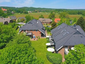 A residential area with houses featuring steep roofs and brick exteriors, surrounded by lush greenery and open fields.
