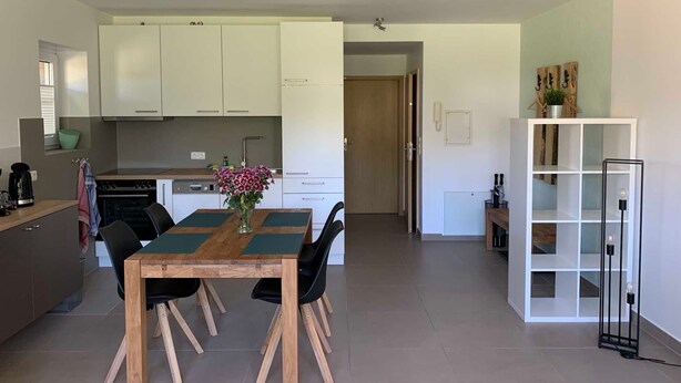A modern kitchen with white cabinets, a dining table with chairs, and a small dining area. - 2-room apartment 22 (H) - Lancken-Granitz apartment complex (Lancken-Granitz)