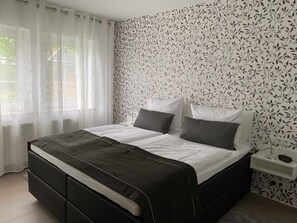 Une chambre moderne avec un lit noir, du linge de lit blanc et un papier peint à motifs floraux.
