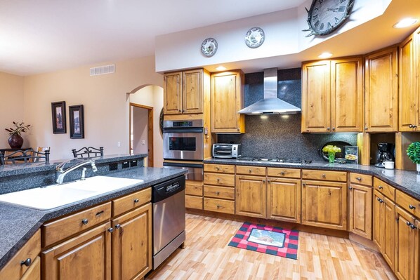 A kitchen with wooden cabinets, stainless steel appliances, a granite countertop, and a red and black checkered rug.