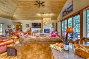 A spacious living room with leather furniture, a stone fireplace, and large windows offering a view of the outdoors.