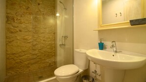 Et badeværelse med stenvæg, toilet, vask og brusebad.