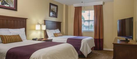 A hotel room with two beds, a ceiling fan, a television on a wooden cabinet, and a window with curtains.