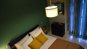 Ett hotellrum med en säng, ett nattduksbord, en lampa och ett fönster med gardiner.