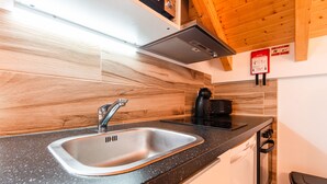 A kitchen with a stainless steel sink, wooden wall paneling, a black coffee maker, and a fire safety sign. - Estúdio-suite com Terraço a 2 Minutos a pé da Praia de Peniche (Peniche)