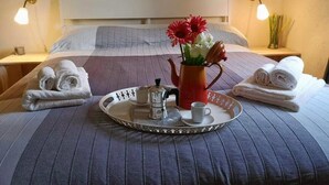 Een net opgemaakt bed met een dienblad met ontbijtartikelen, waaronder een koffiezetapparaat, kopjes en een vaas met bloemen.