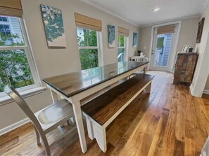 Uma área de refeições com mesa de vidro, banco de madeira e cadeiras.