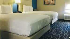 A hotel room with two beds, a nightstand, a lamp, a painting, and a window. - Baymont Inn & Suites by Wyndham (McAllen)