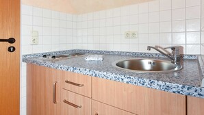 Une cuisine dotée d’un comptoir en granit, d’un évier en acier inoxydable, de meubles en bois et de carreaux de céramique blancs disposés en motif métro sur le mur.