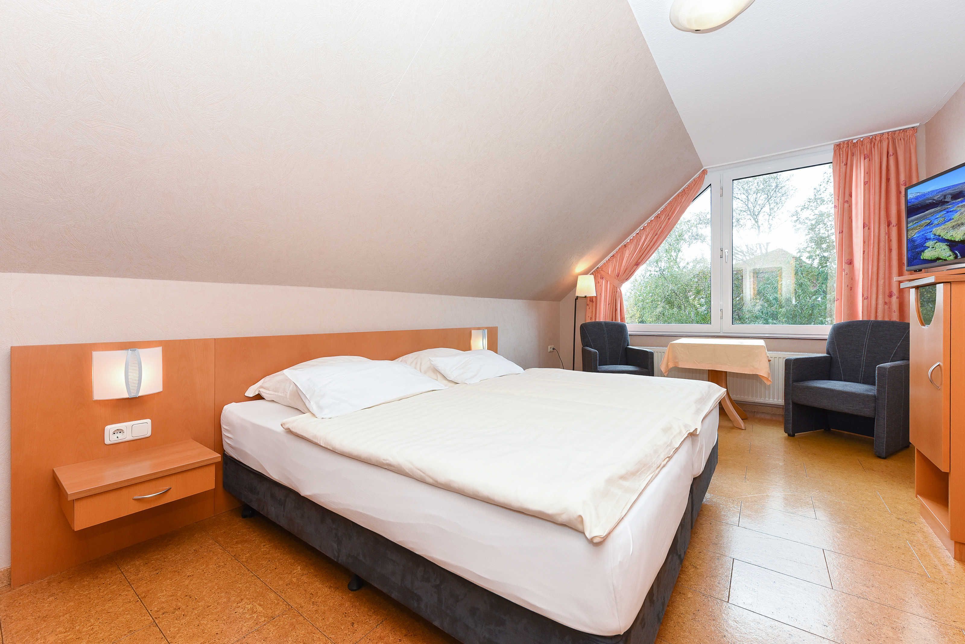 A bedroom with a bed, bedside table, lamp, chair, and a TV.