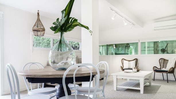 A modern dining area with a wooden table, white chairs, and a glass vase with a plant.