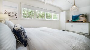 A bedroom with a large bed, a TV, and a window with a view of trees.