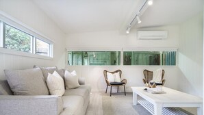 A modern living room with a grey sofa, two wicker chairs, a white coffee table, and a large window providing natural light.